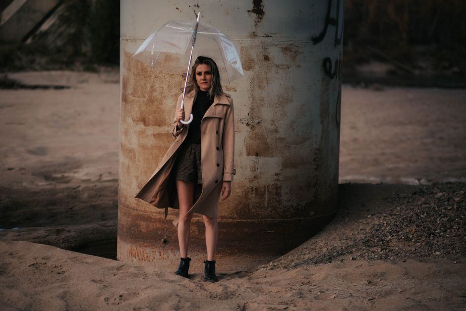 A stylish woman holds an umbrella by a large pillar in an urban landscape.