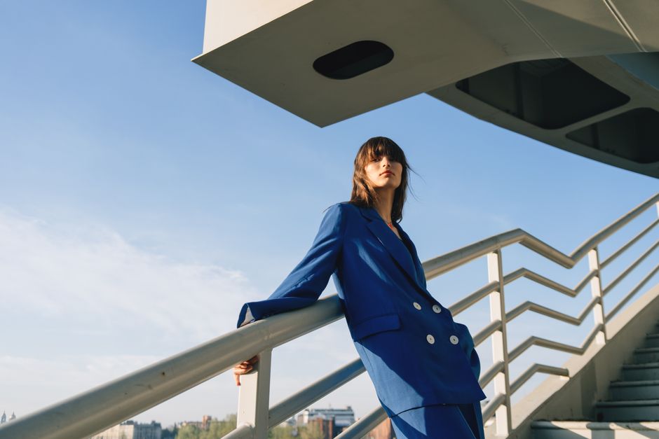 Stylish woman in blue suit posing outdoors against a modern urban backdrop.
