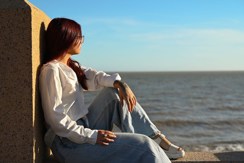 Woman sitting by the sea with relaxed expression on a sunny day