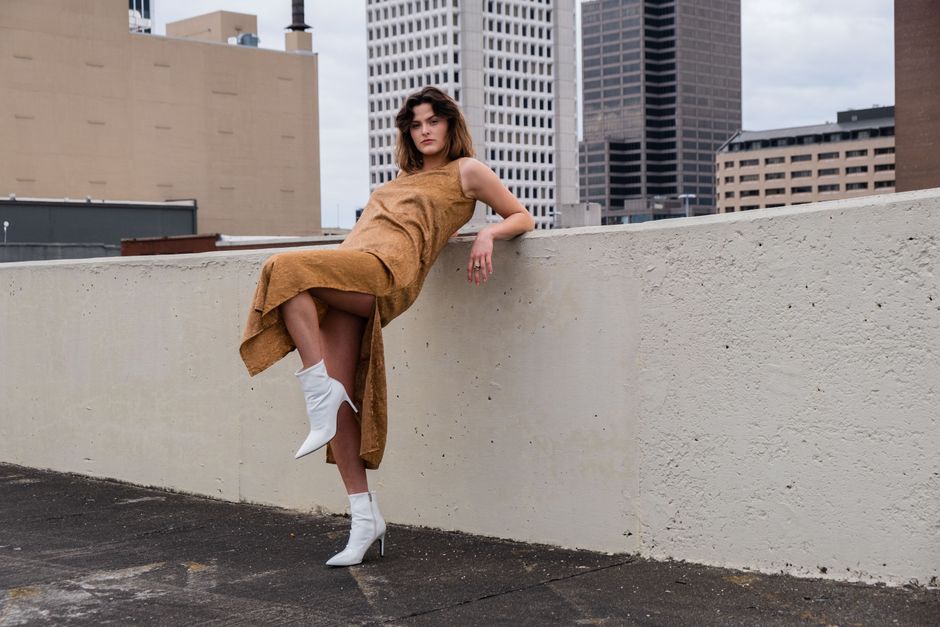 Stylish woman in fashionable dress posing on a rooftop with city skyline backdrop.