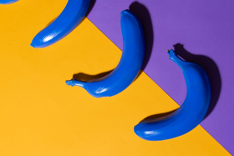 Creative image of blue bananas on a vivid yellow and purple backdrop, illustrating conceptual art.