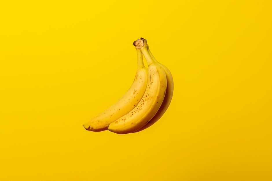 A bunch of ripe yellow bananas against a vivid yellow backdrop, offering tropical freshness.