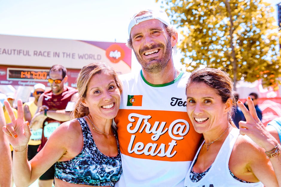 Three runners proudly celebrate finishing a marathon together with smiles and peace signs.