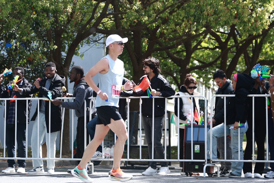 A marathon runner passes a cheering crowd outdoors on a sunny day.