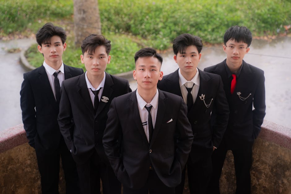 A group of five young men in formal suits posing outdoors, exuding confidence.