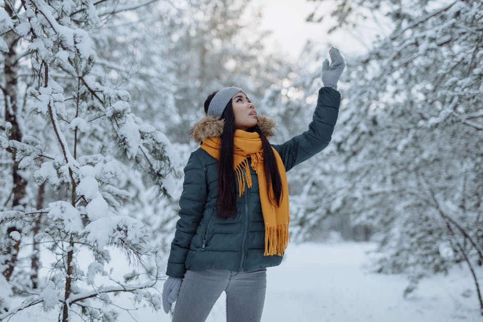 A woman enjoys a snowy winter day in the forest wearing a warm jacket and scarf.