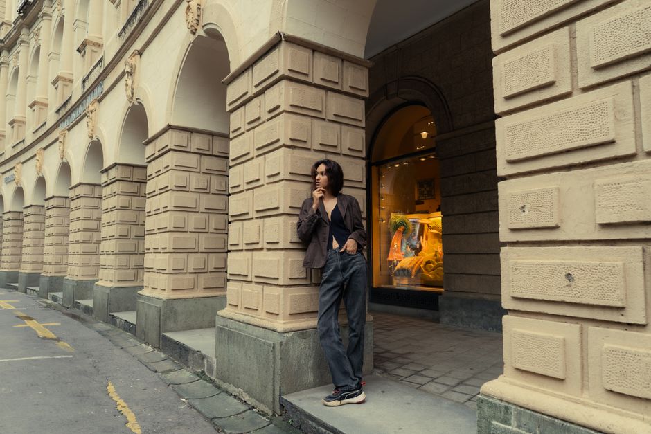 Person standing by arched historic architecture, embodying a relaxed urban style.