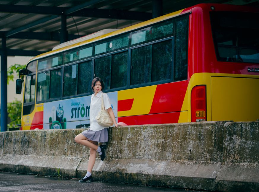 Woman standing by a colorful bus under a shelter on a rainy day.