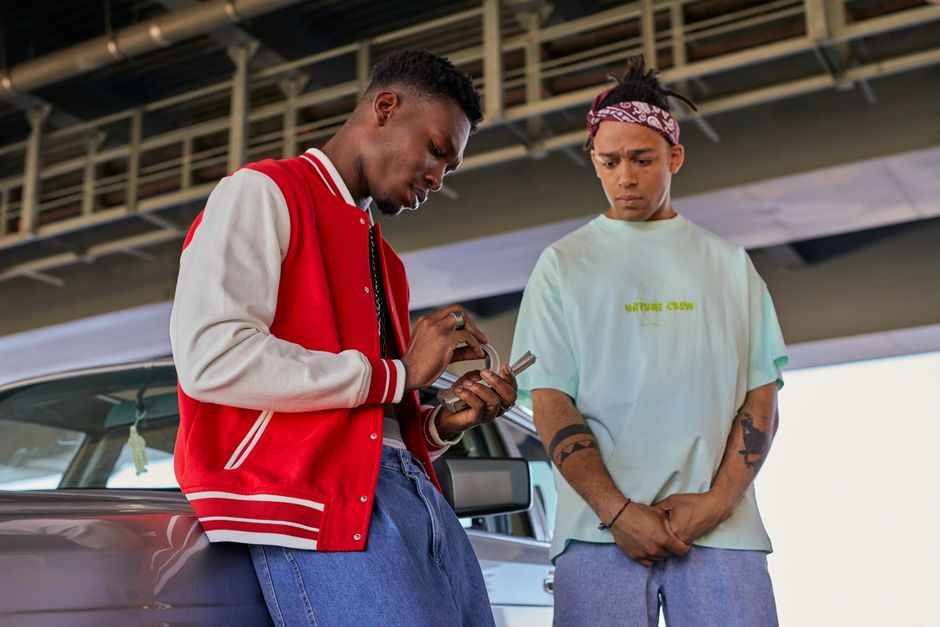 Two fashionable men in streetwear counting cash under a bridge.