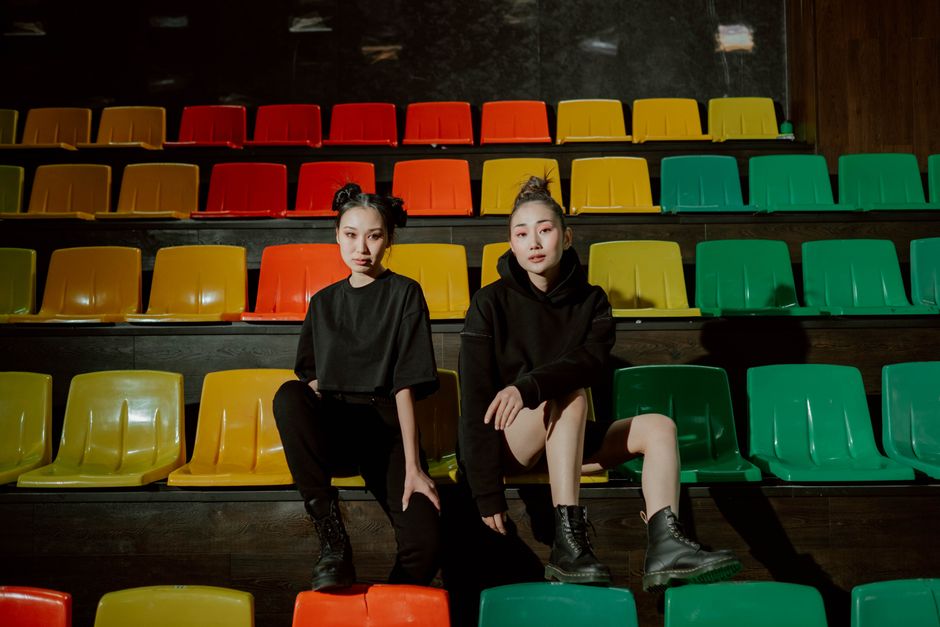 Two women in black outfits sitting on vibrant stadium seats, showcasing modern fashion and style.