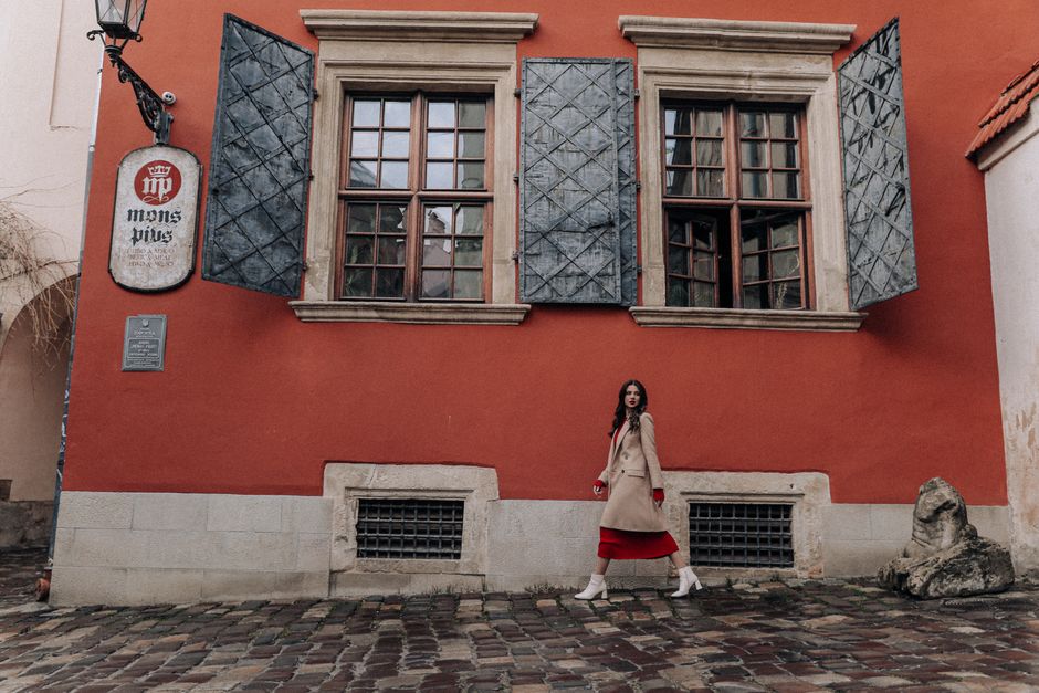 Stylish woman in coat walking by an old town building on cobblestone street.