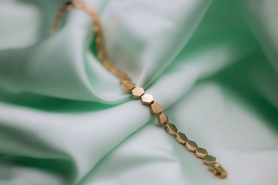 Close-up of a stylish gold bracelet on soft mint-colored fabric with selective focus.