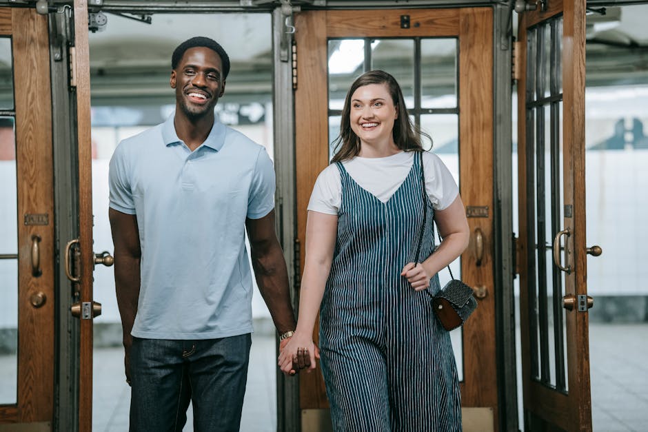 Smiling interracial couple holding hands while walking indoors, radiating happiness and love.