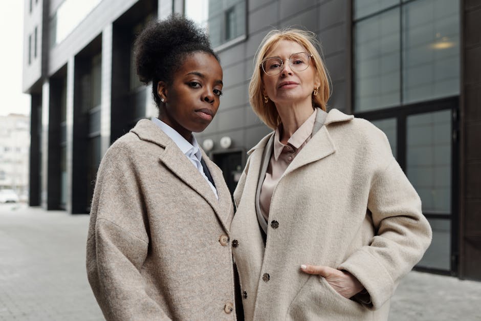 Two diverse businesswomen in stylish coats posing confidently on a city street.