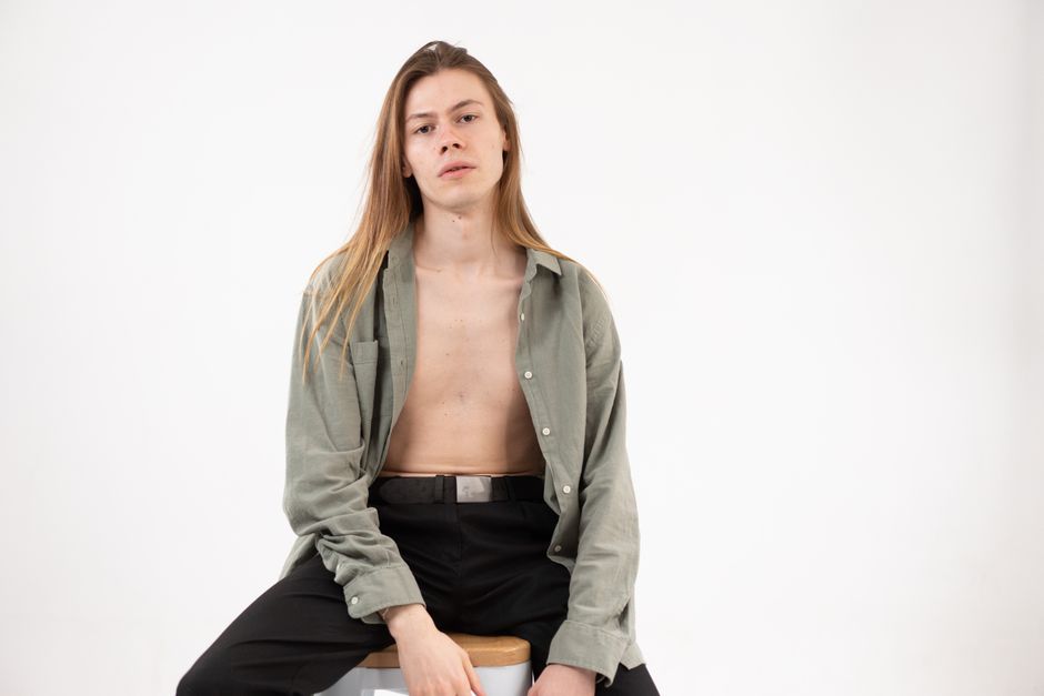 Stylish portrait of a long-haired person sitting on a stool in a studio setting.