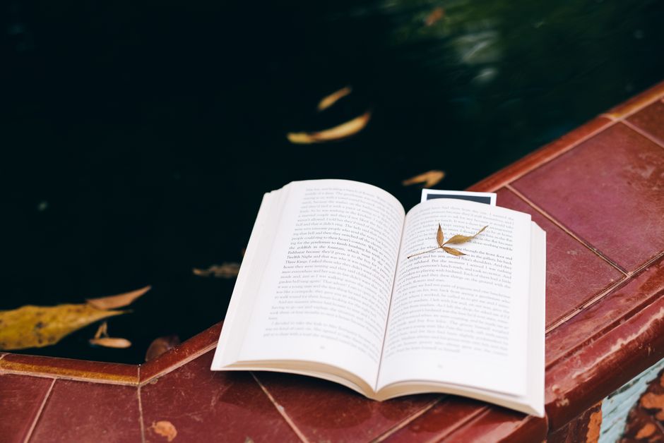 An open book with a leaf on a poolside, capturing a calm autumn moment.
