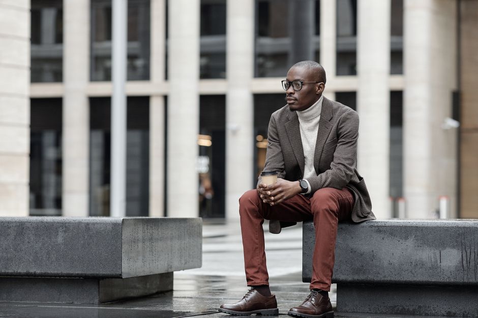Man in a blazer and turtleneck sitting outside an office building