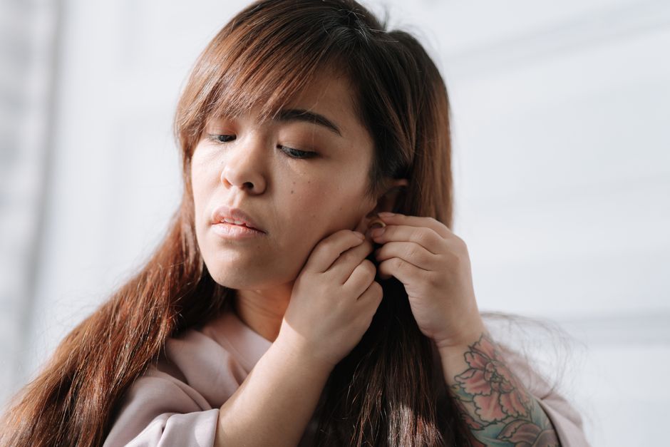 A woman wearing earrings in a bright, airy room, showcasing morning routine and personal expression.