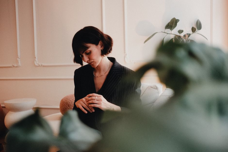 A thoughtful woman in a stylish room, surrounded by plants and elegant decor, conveys a reflective mood.