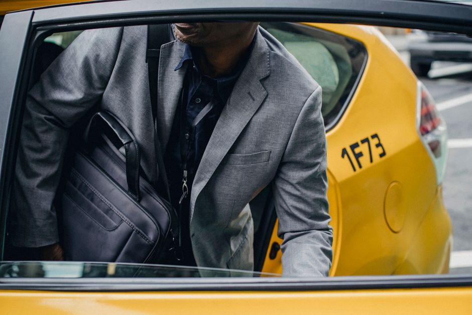 Crop unrecognizable African American male in classy jacket sitting in yellow taxi parked on busy city street