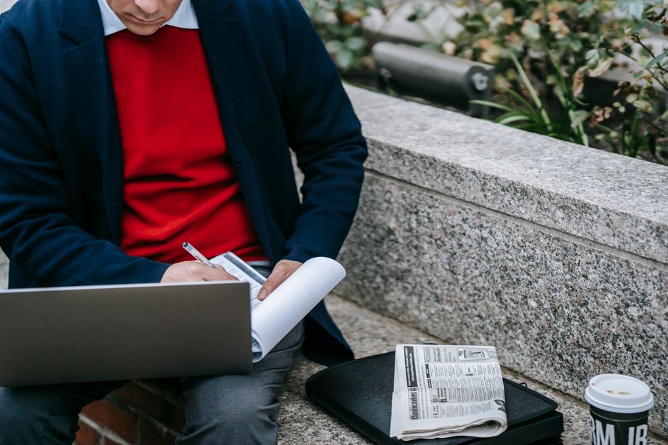 A professional man multitasking with a laptop and documents in an outdoor setting, blending technology and business.