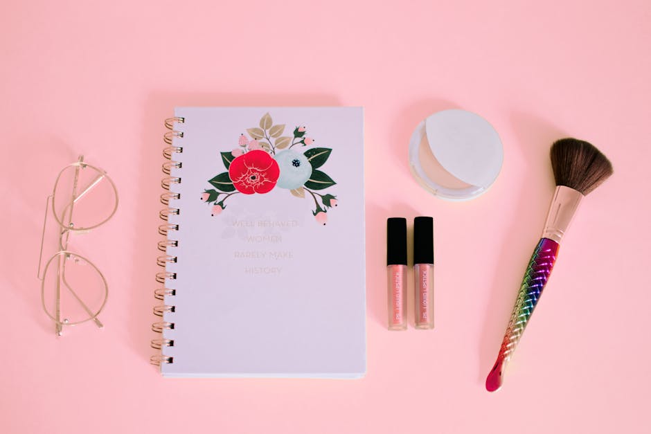 Beauty flat lay with makeup and notebook on a pink surface, perfect for girly themes.