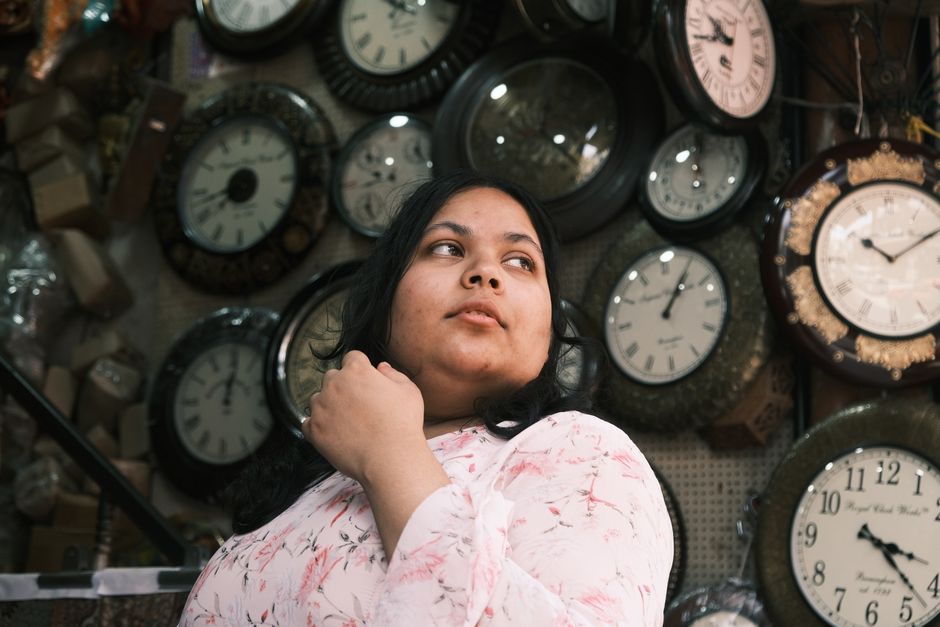 Woman posing thoughtfully in a Bengaluru shop surrounded by various wall clocks.