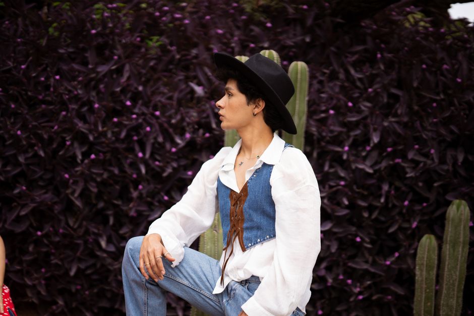 Fashionable person posing outdoors in denim and white, surrounded by vibrant greenery.