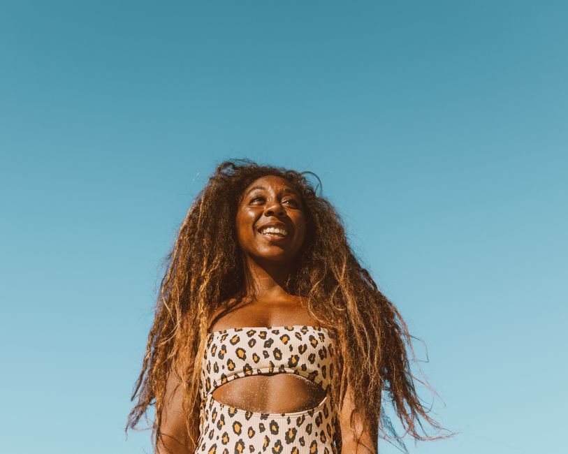 A joyful woman with long hair in a leopard print swimsuit under a clear blue sky.