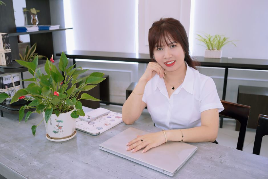 Professional woman smiling at desk with laptop and plants in a bright office setting.