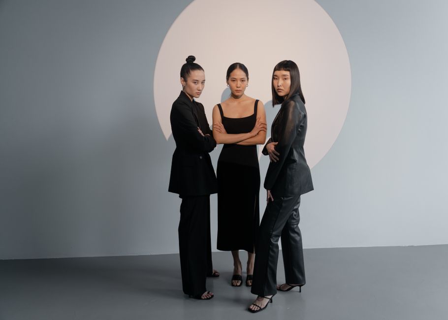 Stylish portrait of three women in black fashion against a minimalist backdrop.