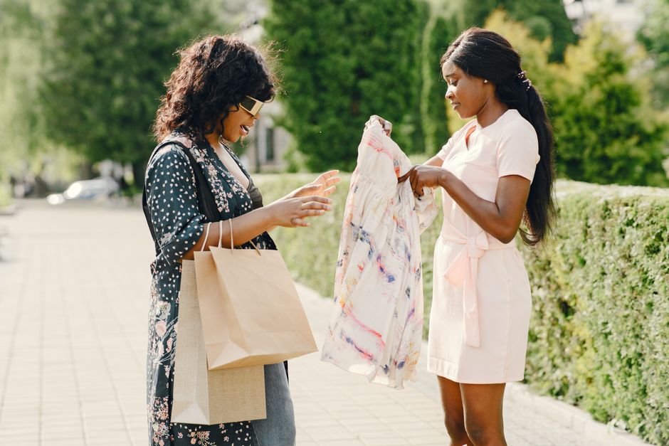 Two women outdoors discussing clothes while shopping, showcasing fashion trends.