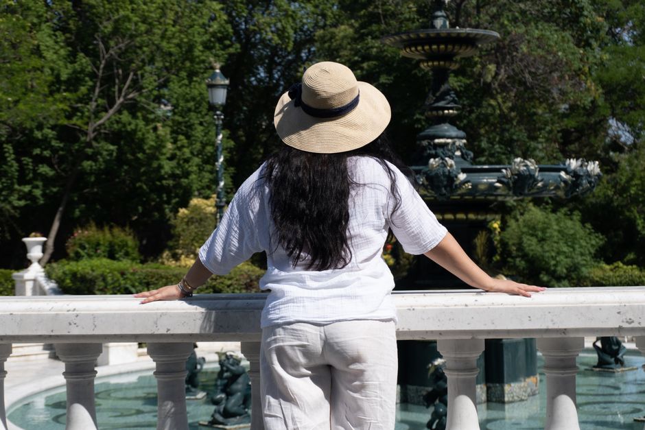 A woman with a sun hat enjoys a summer day by a decorative fountain in a lush park in Baku, Azerbaijan.
