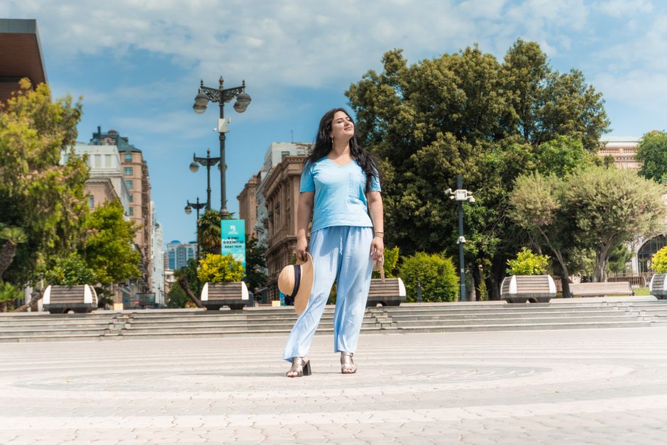 A young woman enjoys a peaceful walk on Baku Boulevard, embracing the morning light with a straw hat in hand.