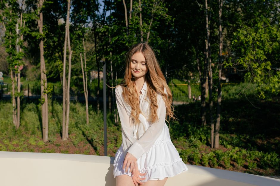 A young woman in a white dress enjoys a sunny day in a green park.