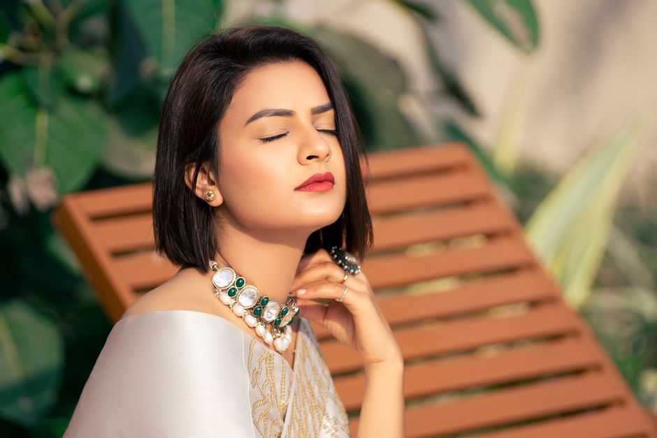 A stylish woman with jewelry enjoys a sunny moment outdoors.