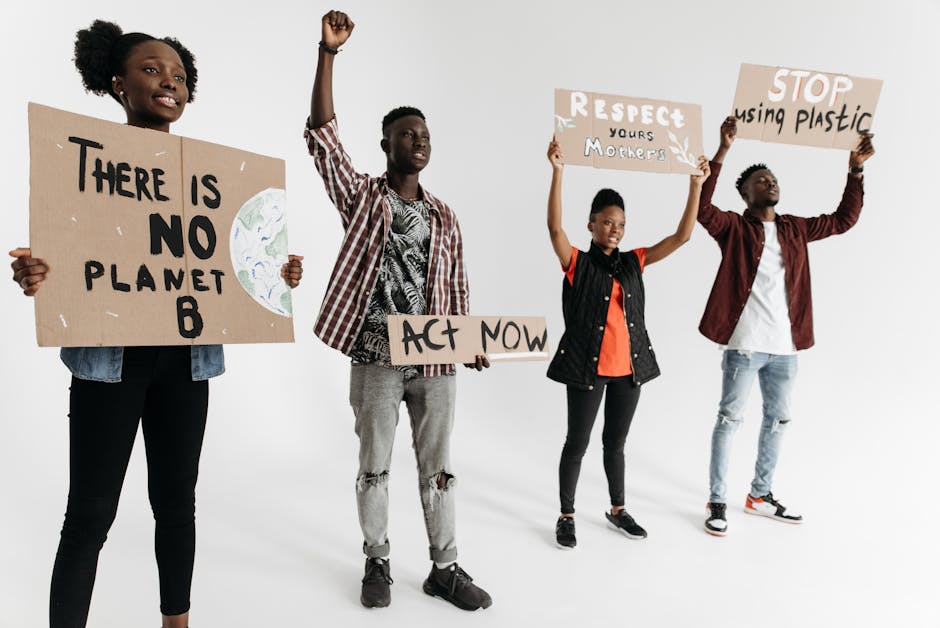 Diverse group of young adults holding environmental protest signs indoors on a white background.