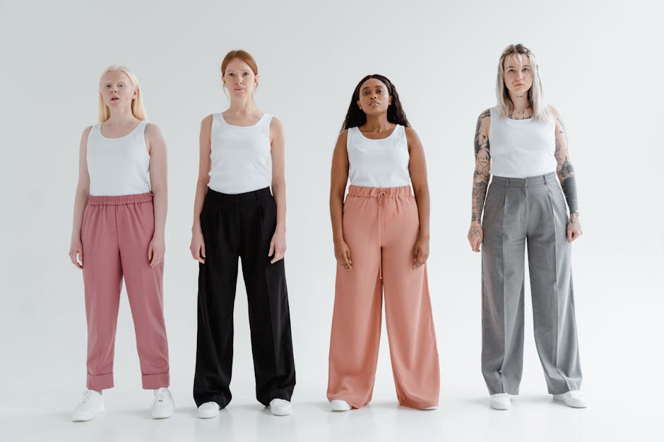 Four diverse women stand confidently in stylish pants and white tank tops against a white backdrop.