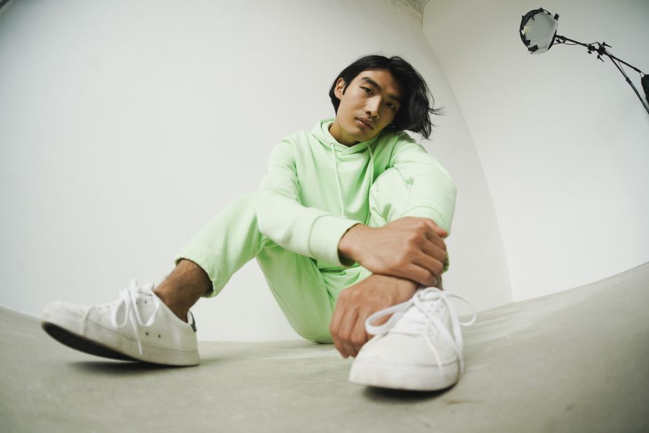 Low-angle shot of a man in a green hoodie posing stylishly in a studio setting.