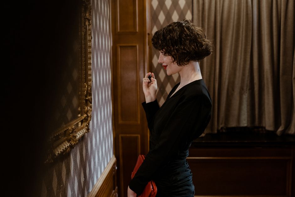 A stylish woman in a black dress admiring art in a sophisticated indoor setting.